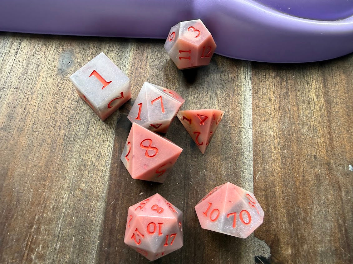 Pink polyhedral dice set on a wooden surface