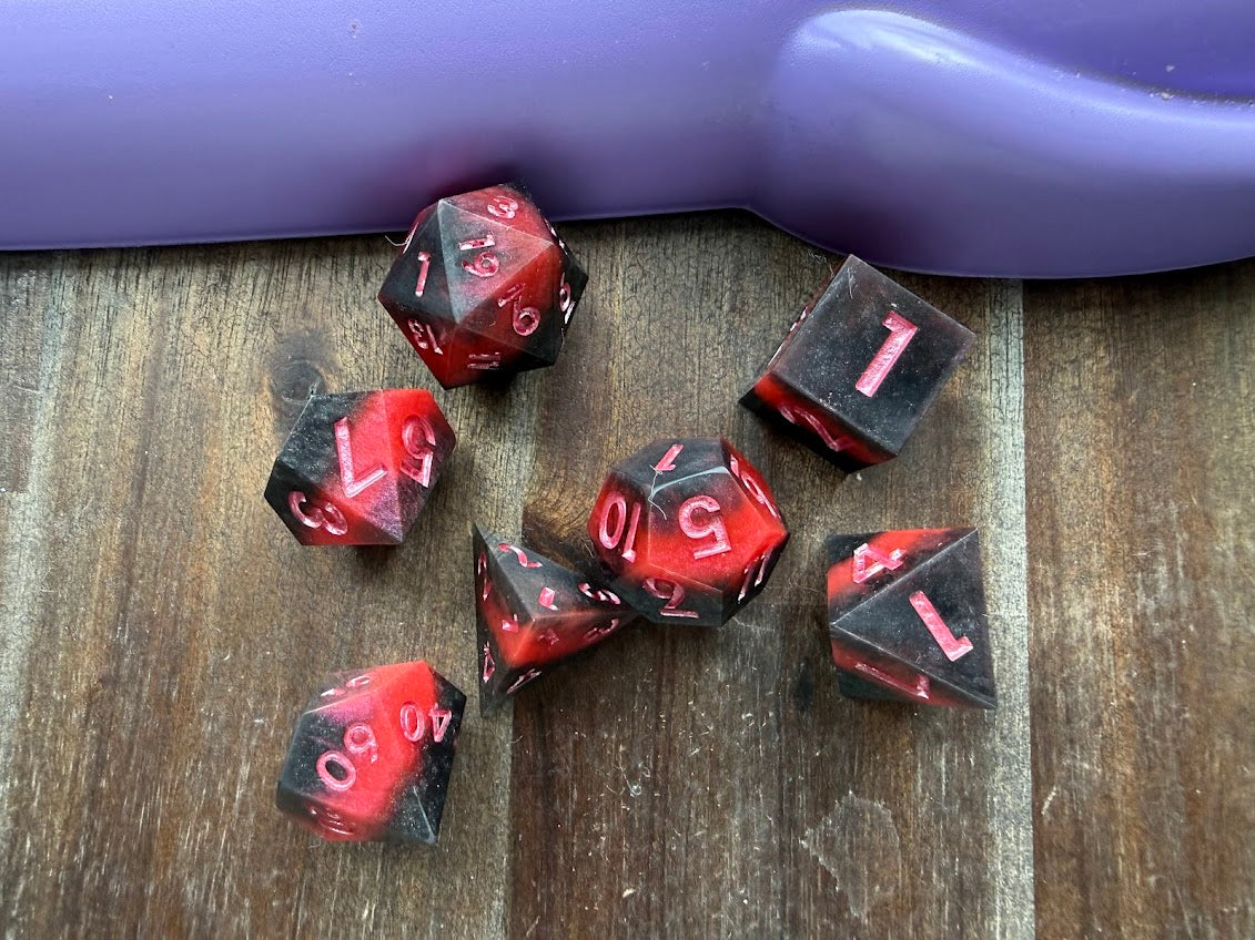 Set of red and black dice on a wooden surface with a purple object in the background.