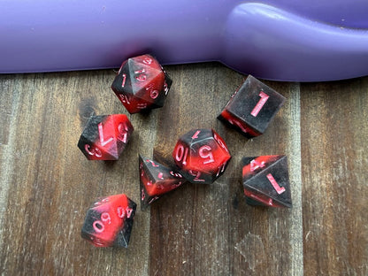 Set of red and black dice on a wooden surface with a purple object in the background.