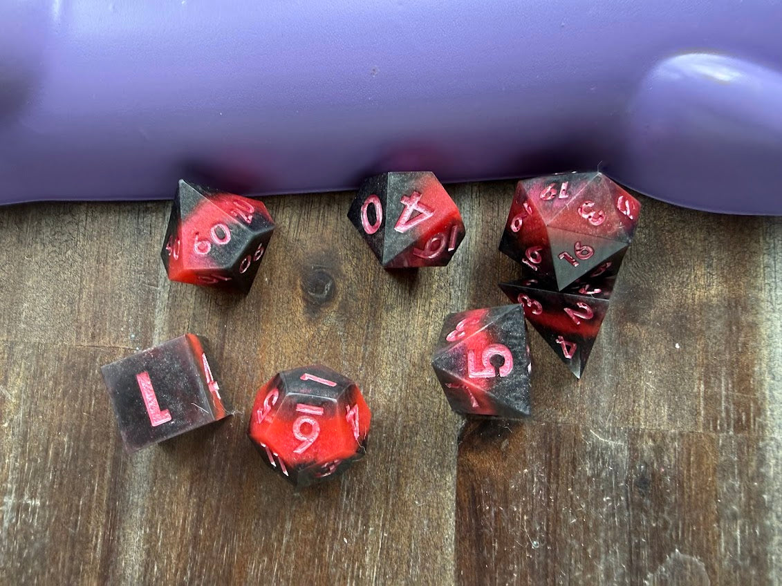 Set of red and black dice on a wooden surface with a purple object in the background.