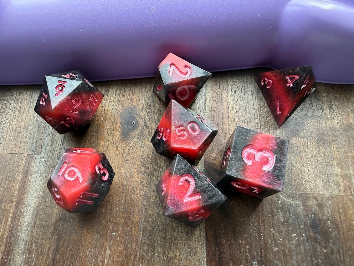 Set of red and black polyhedral dice on a wooden surface with a purple background