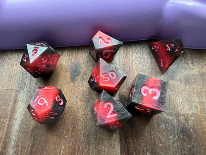 Set of red and black polyhedral dice on a wooden surface with a purple background
