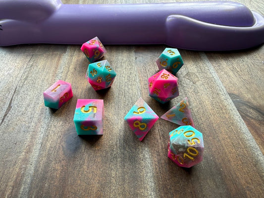 Set of copper-colored polyhedral dice on a wooden surface with a purple object in the background.