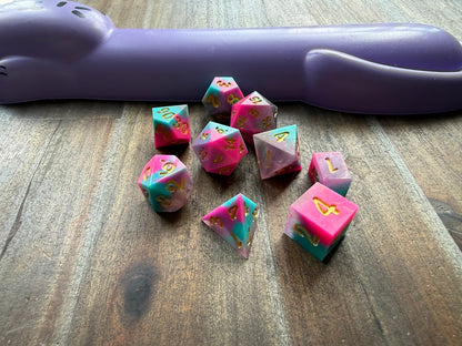 Set of polyhedral dice on a wooden surface with a purple handle in the background.