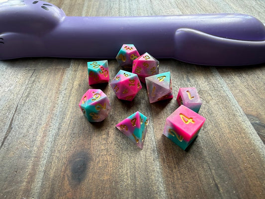 Set of polyhedral dice on a wooden surface with a purple handle in the background.