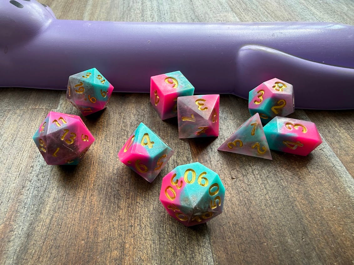 Set of polyhedral dice on a wooden surface with a purple handle in the background.