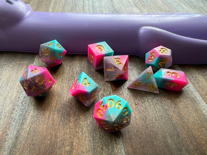 Set of polyhedral dice on a wooden surface with a purple handle in the background.