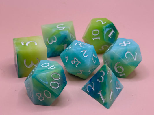 A set of seven green, blue and white dice on a pink surface.