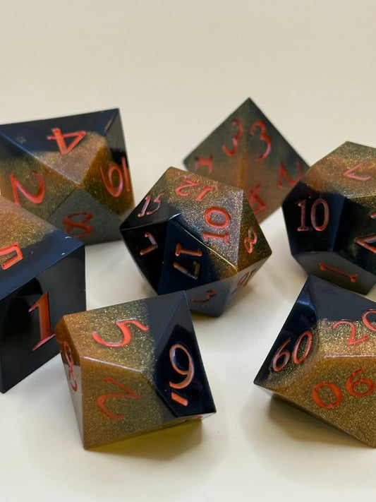 Set of black and gold polyhedral dice with metallic sheen on a white background