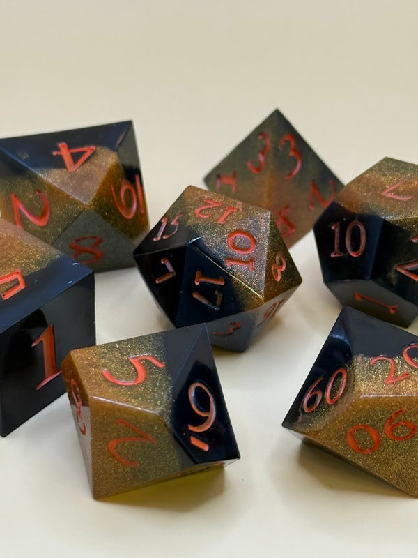 Hand-poured polyhedral dice set in black and gold with red numbers on a light background