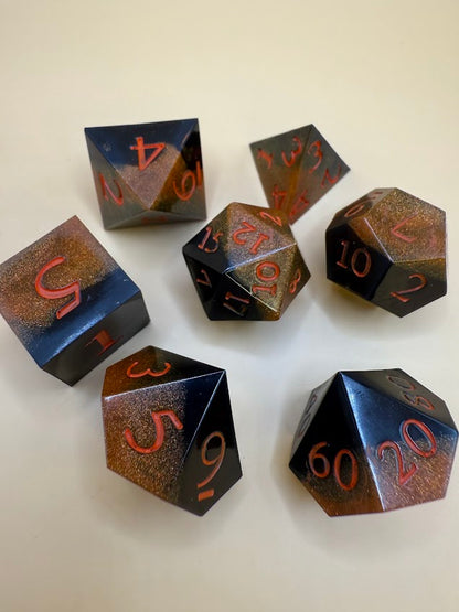 Set of black and gold polyhedral dice with metallic sheen on a white background