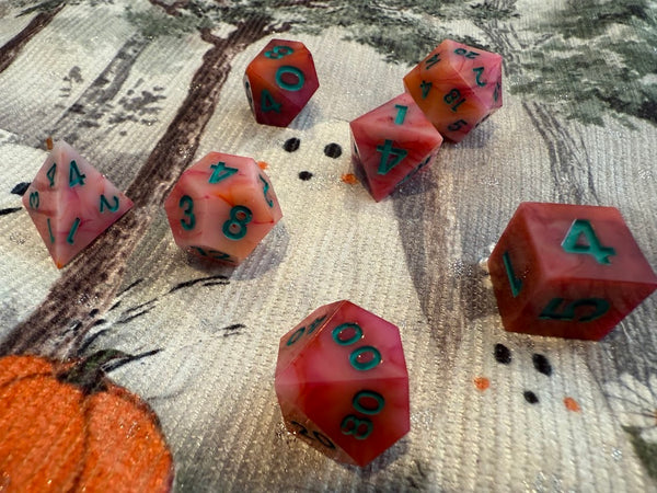 Set of red and pink hand-poured polyhedral dice with green numbers on a fantasy-themed cloth