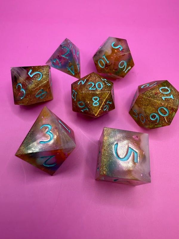 Handmade resin polyhedral dice set with gold shimmer and blue numbers on pink background
