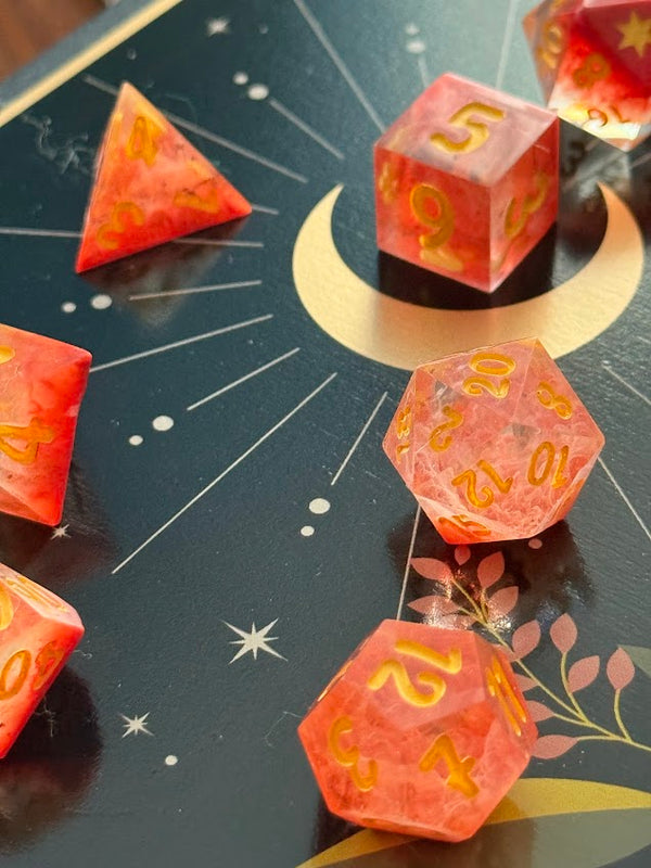 Hand-poured red resin dice set with gold numbers on a celestial tarot card background.