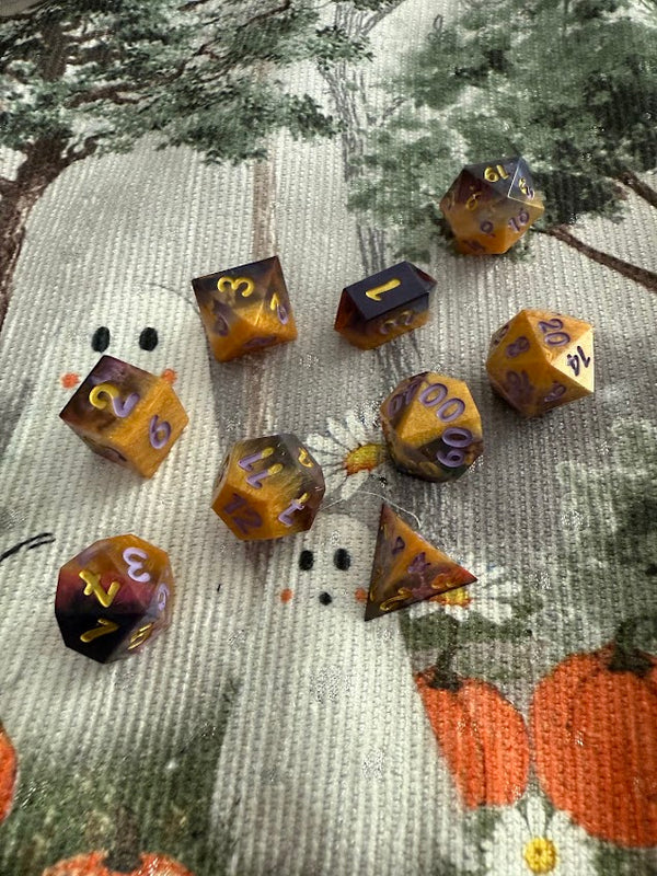 Handmade orange and purple polyhedral resin dice set with gold numbers on a Halloween themed mat