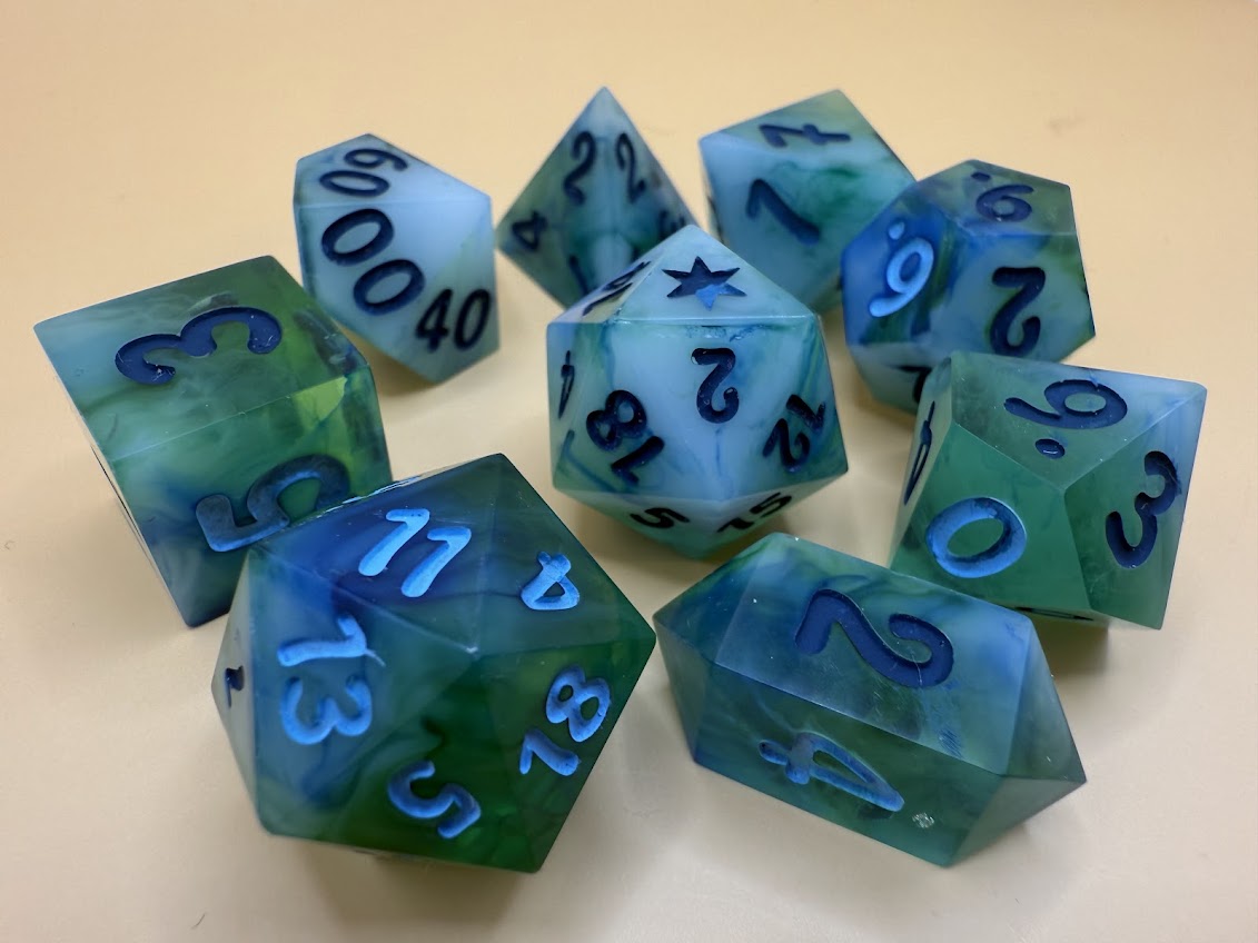 Set of blue and green polyhedral dice with black numbers on a beige background