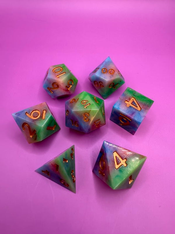 Colorful polyhedral resin dice set with gold numbers on a pink background