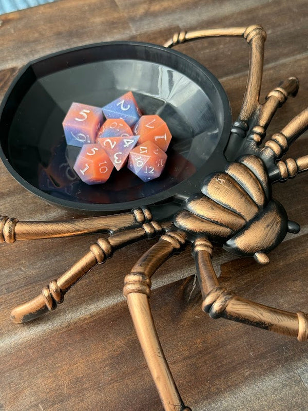 Red and blue polyhedral dice in a spider-shaped dice tray on a wooden table