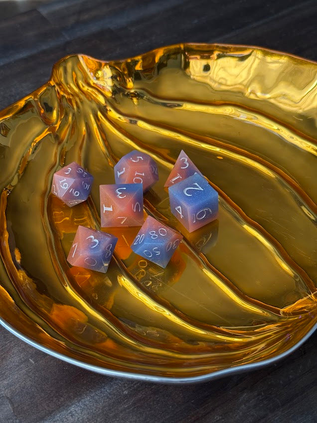 Set of polyhedral dice with blue and pink faces on a gold metallic surface.