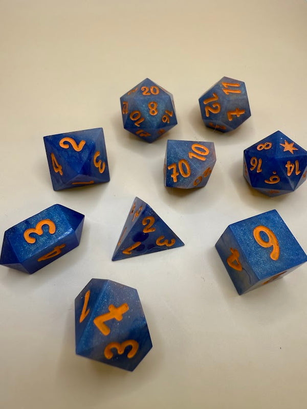 Blue polyhedral dice set with orange numbers on a light background, tabletop RPG dice.