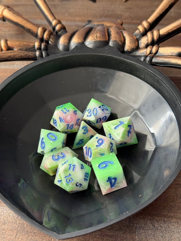 Set of green and pink polyhedral dice with blue numbers in a black spider-themed tray