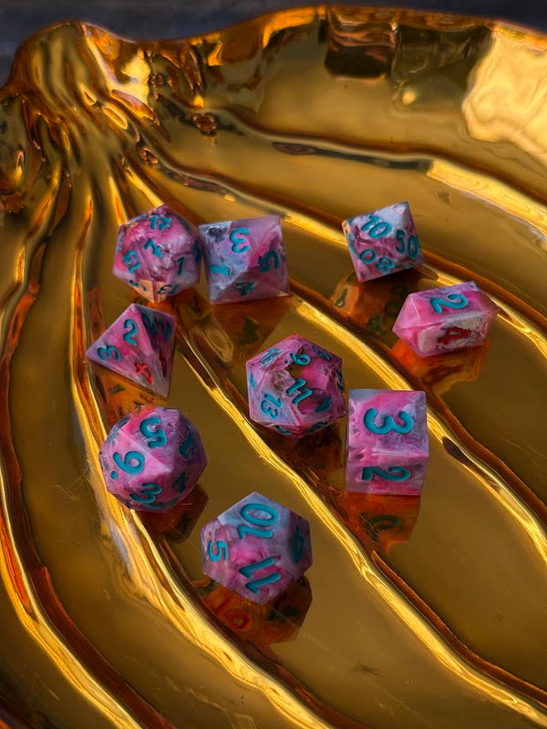 Handcrafted pink resin polyhedral dice with teal numbers on a gold tray
