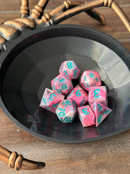 Pink and teal dice with numbers on a black dish