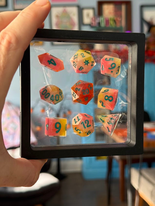 Colorful dice set in a clear plastic case held by a hand with a blurred indoor background