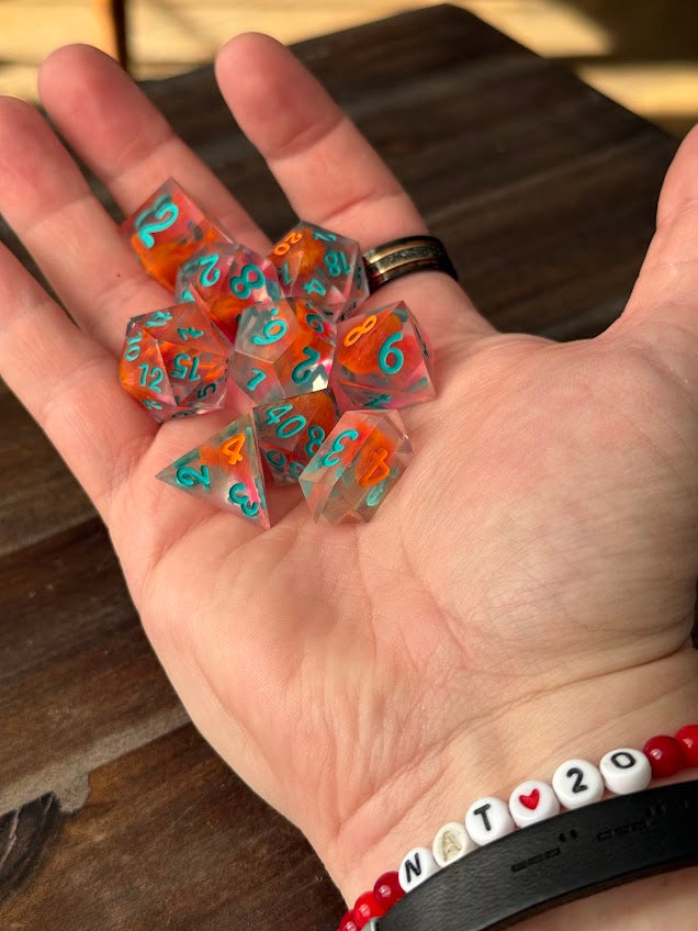 Hand holding a set of clear resin polyhedral dice with red swirls and teal numbering