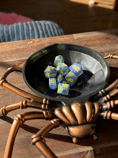Handmade blue and yellow polyhedral dice set in a black spider-shaped dice tray on wood table