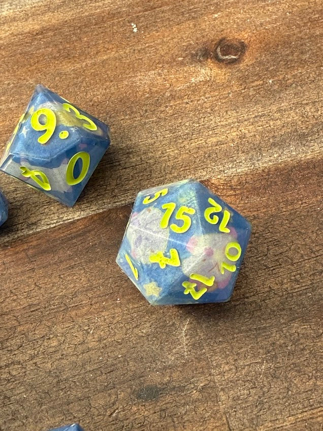 Handcrafted blue resin dice with yellow numbers and star accents on wooden surface