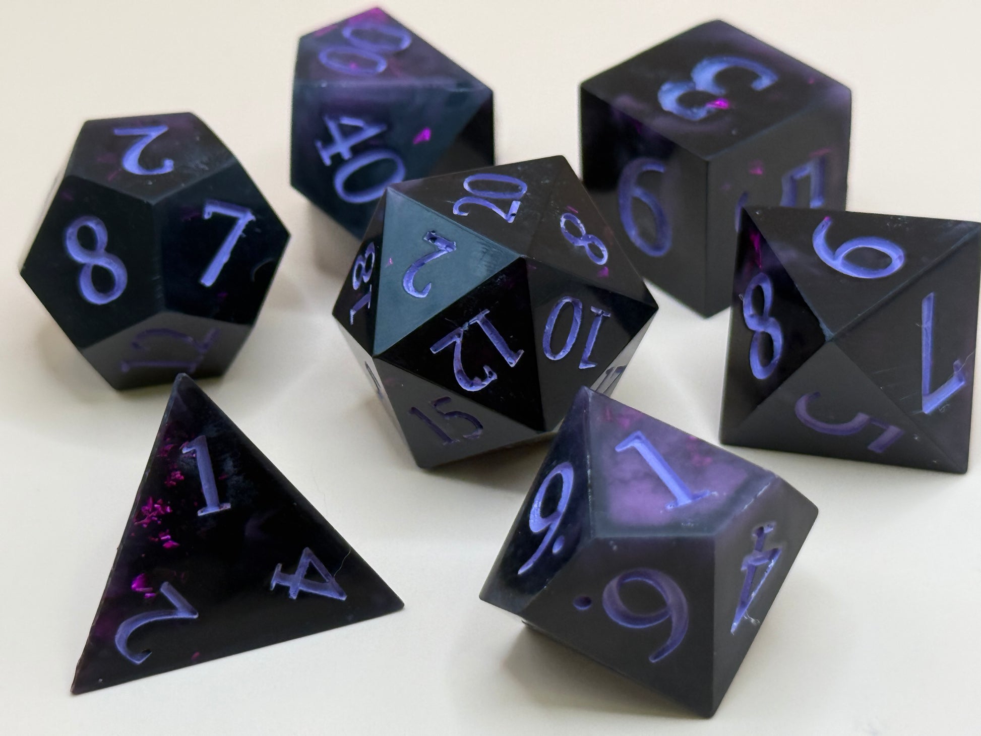 Set of black polyhedral dice with purple numbering on a white background