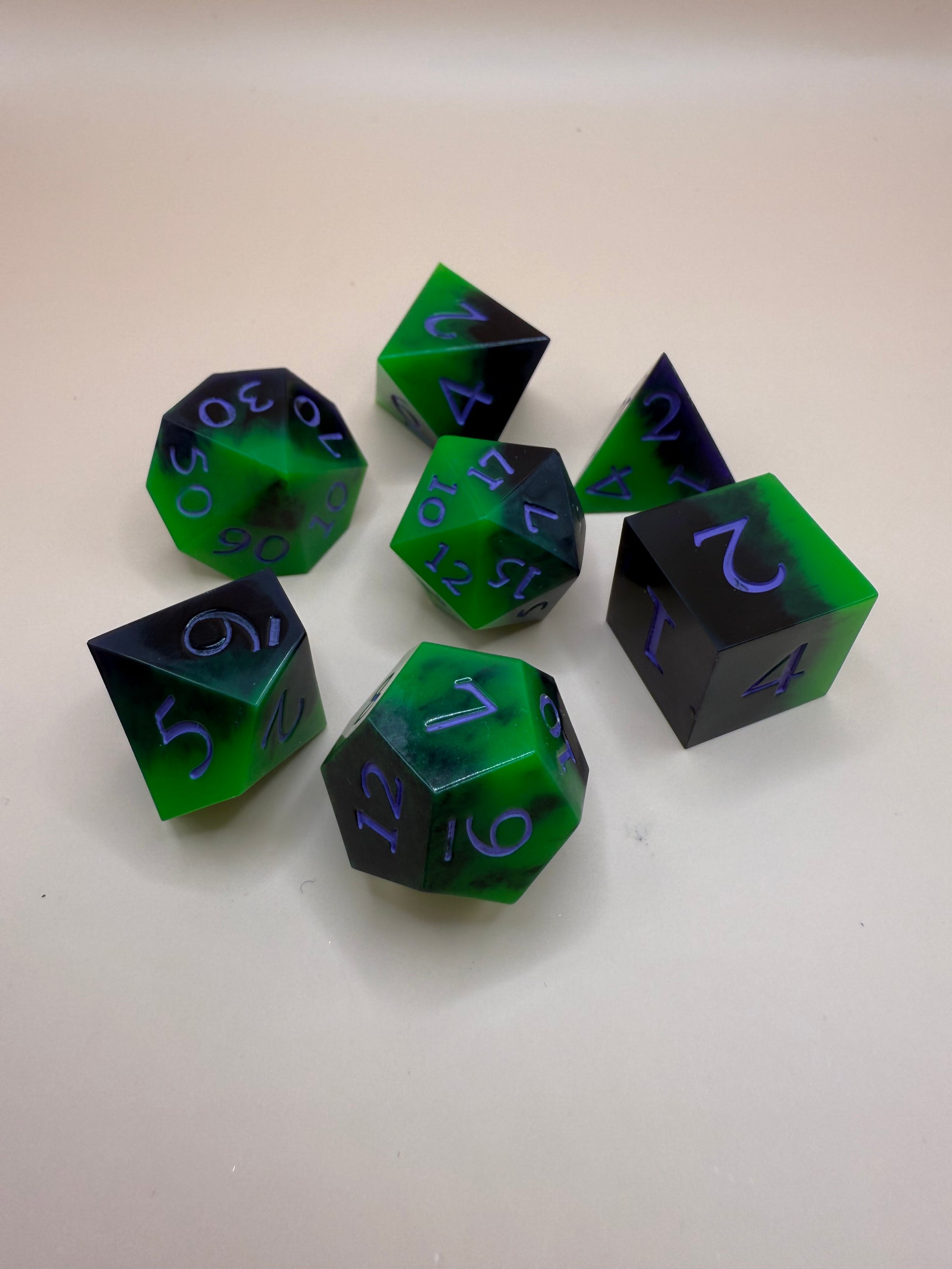 Green and black, sharp-edge dice, set of seven on a white surface. 
