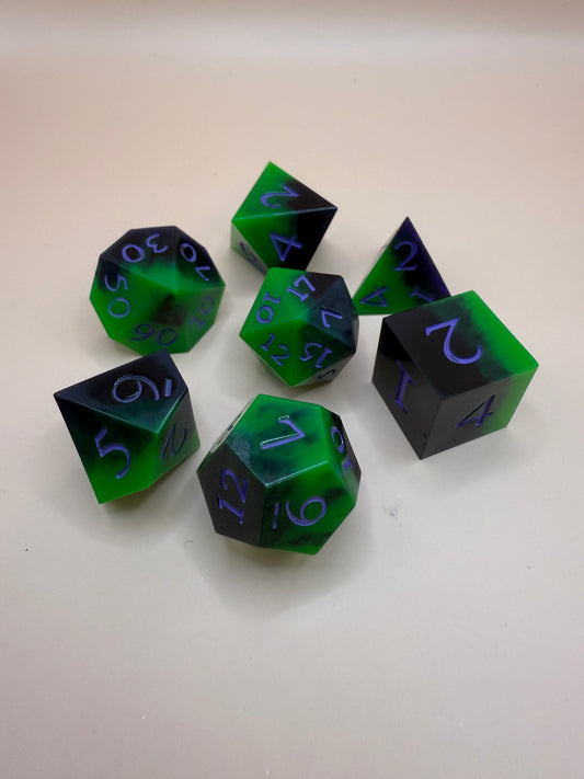Green and black, sharp-edge dice, set of seven on a white surface. 