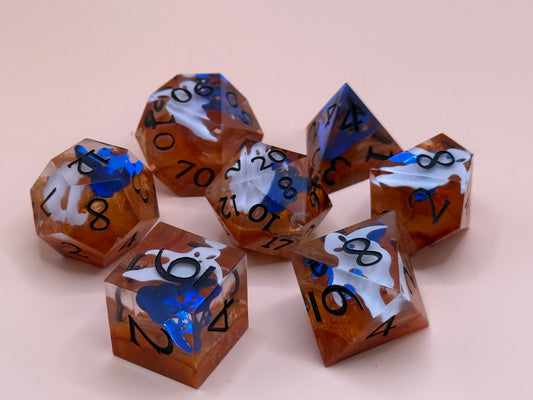 Orange sharp-sided, seven polyhedral dice with ghosts inside of them on a white surface.