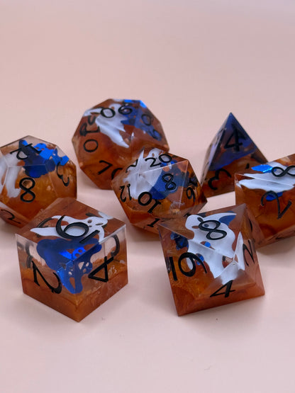 Orange sharp-sided, seven polyhedral dice with ghosts inside of them on a white surface.