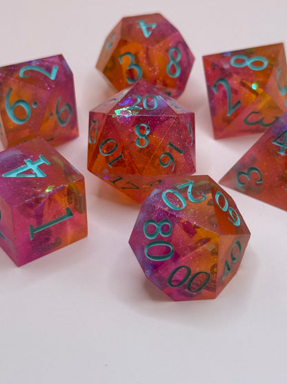 A set seven, D&D hand-poured, resin dice in orange, pink and white , with flecks of glitter, on a wooden table. Numbers inked in teal.