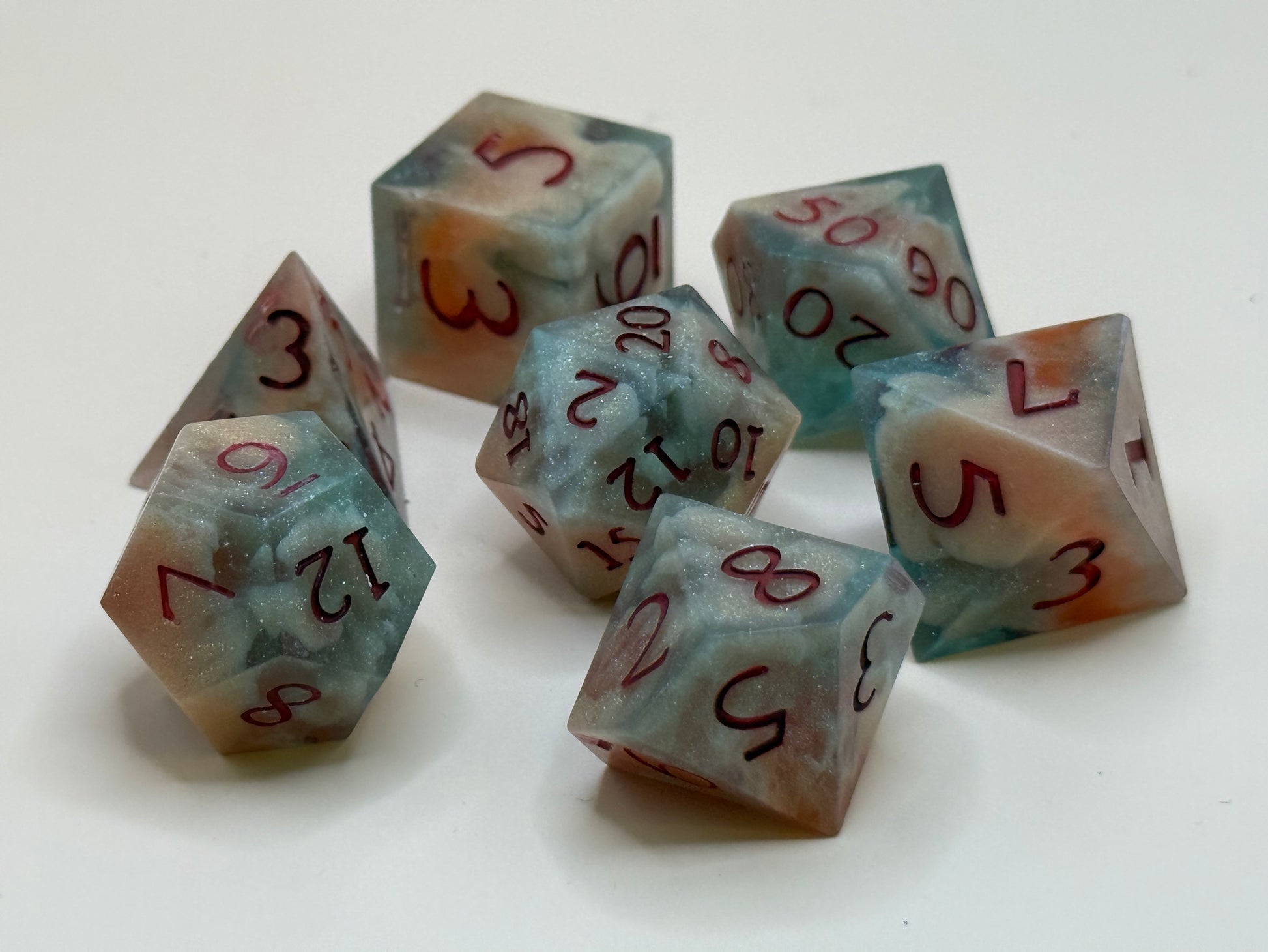 polyhedral sharp-edge, a set of seven in  red, green and bone white held in hands. Numbers are inked in red.