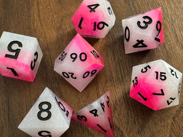 Handmade pink and white resin dice set for tabletop gaming on wooden surface
