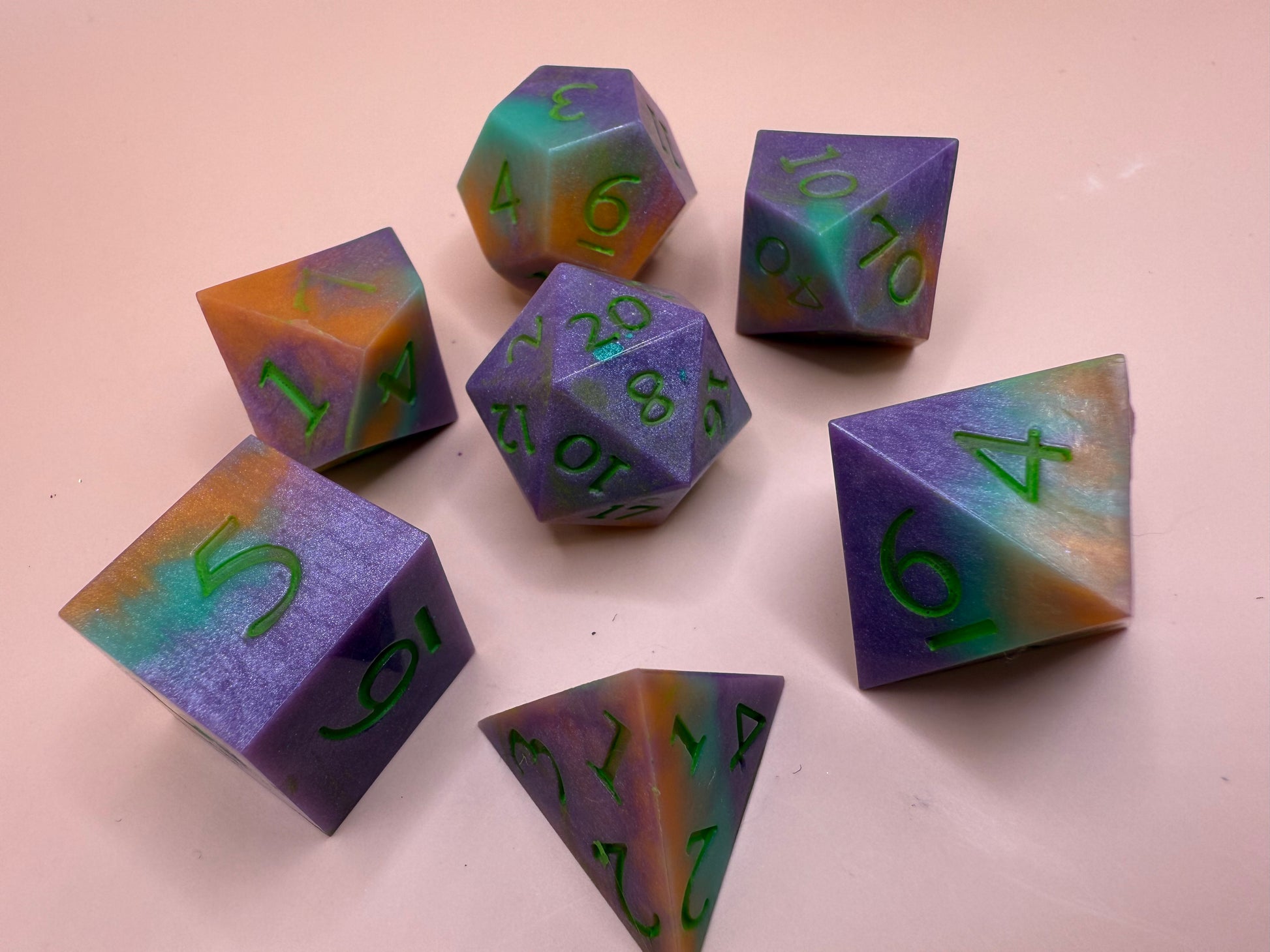 Set of colorful polyhedral dice with green numbers on a light pink background