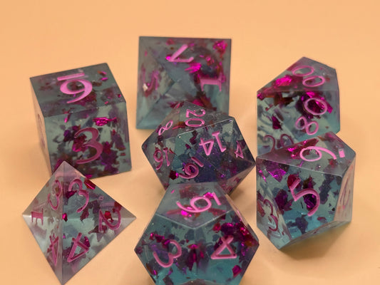 Transparent light blue sharp-edge resin dice with flecks of purple foil on a table.