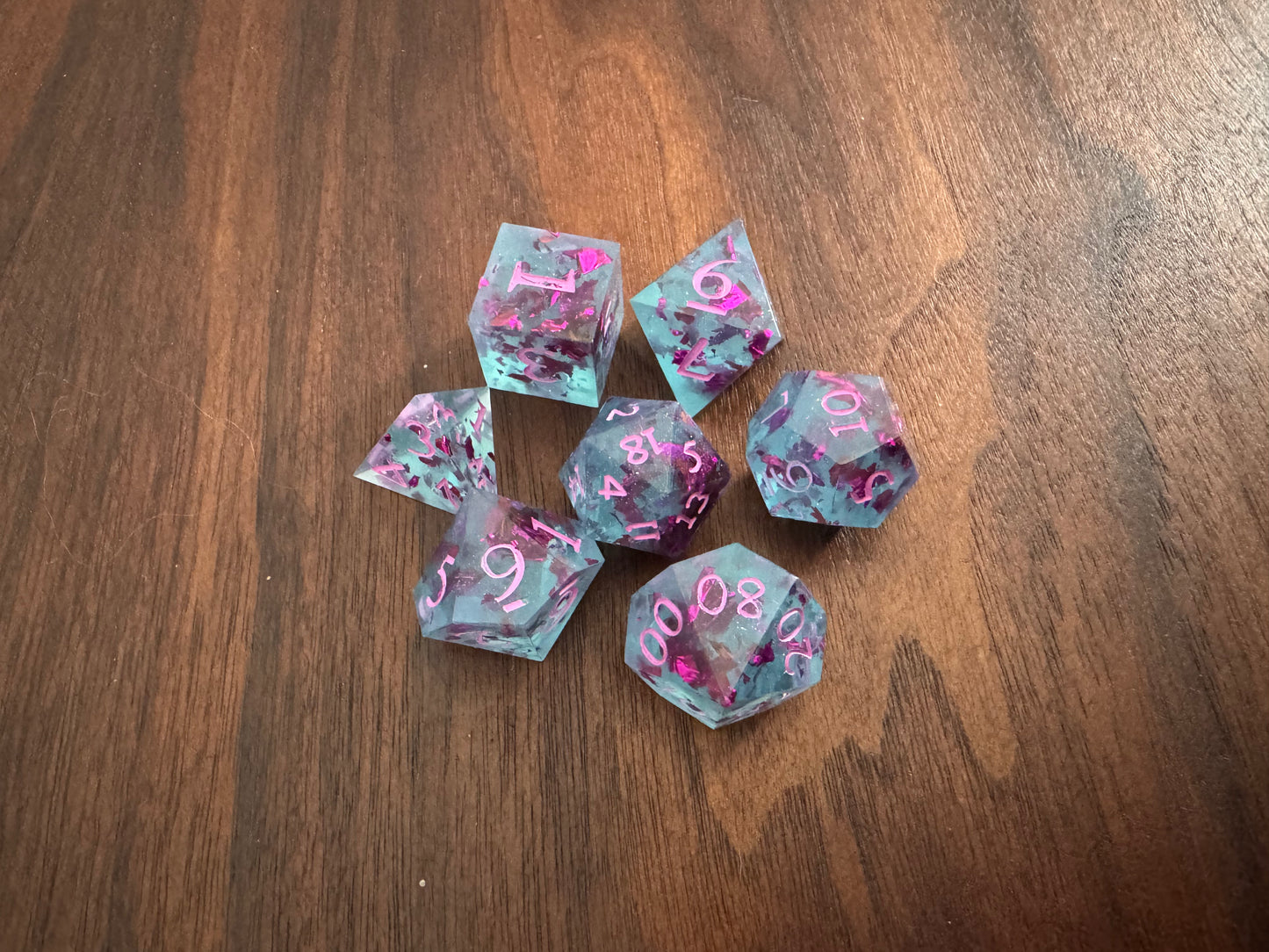 Transparent light blue sharp-edge dice with flecks of purple foil on a table.