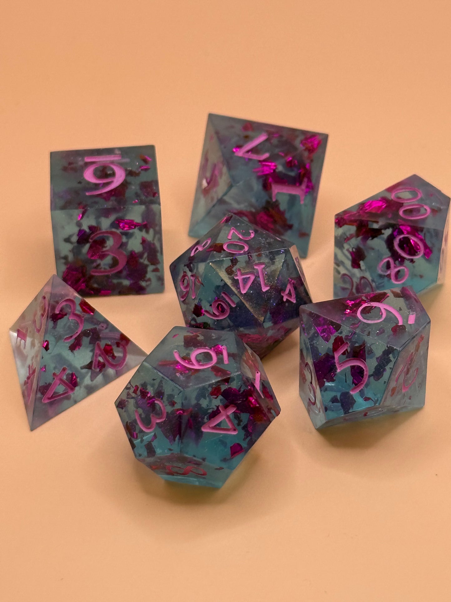 Transparent light blue sharp-edge resin dice with flecks of purple foil on a table.