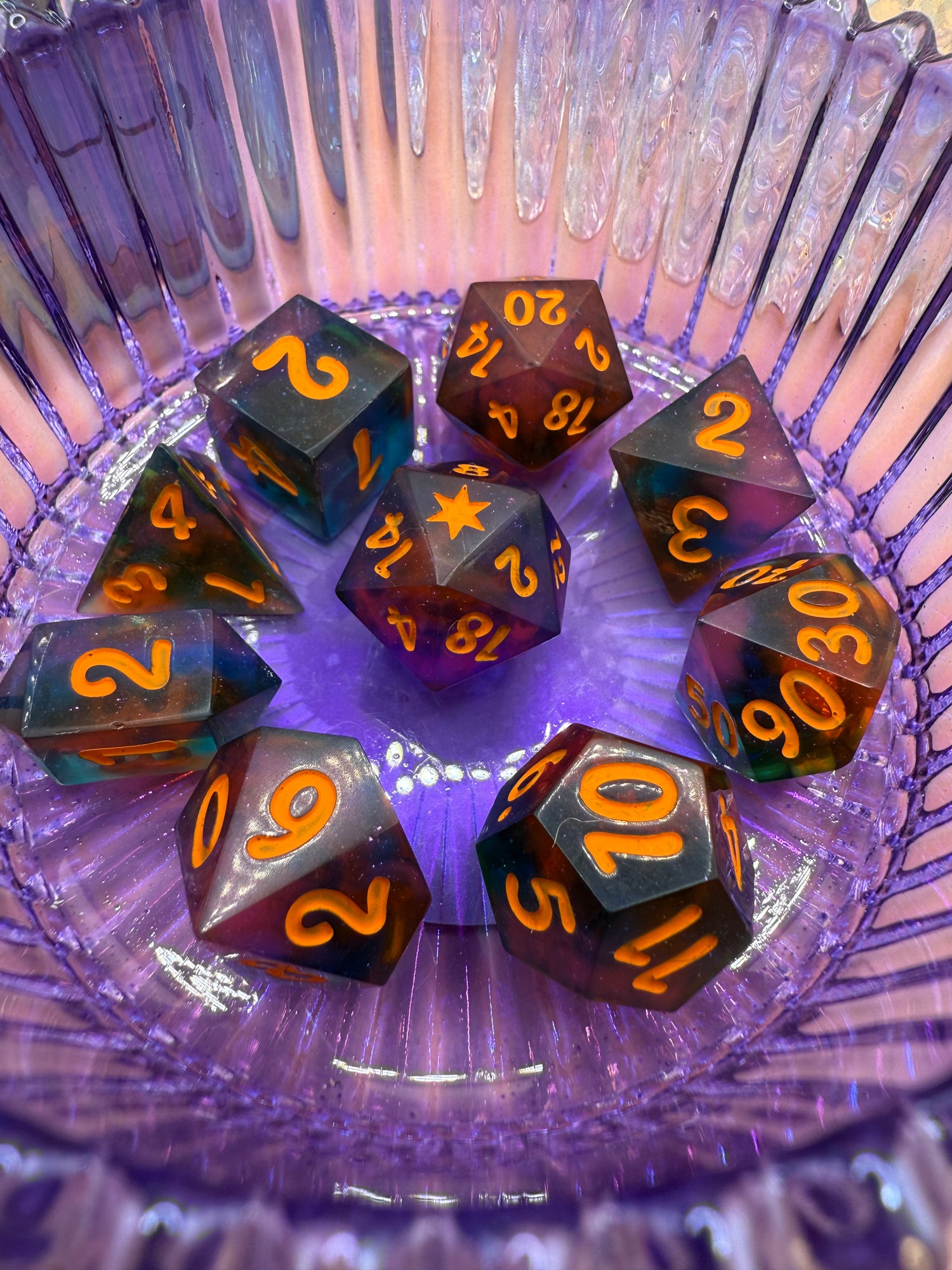 Set of colorful polyhedral dice with orange numbers on a purple glass dish