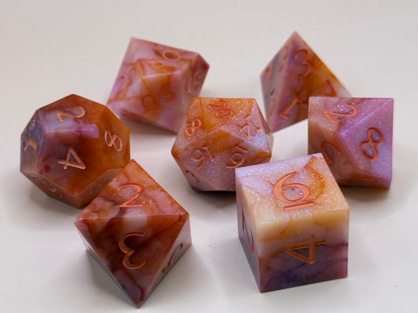 Set of sharp-edged polyhedral dice in orange, pink, and yellow swirls on a plain background