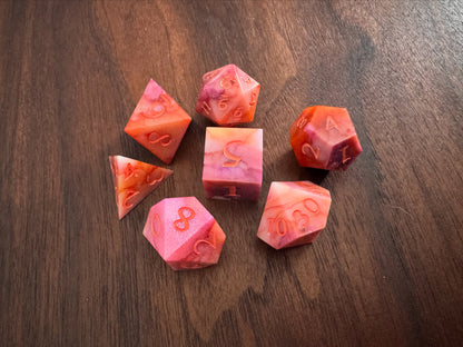 Orange, pink, and white, marbled sharp-edge hand-poured resin dice displayed on a table. 
