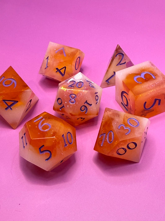 Seven hand-poured orange, pink, and white D&D resin dice on a wood table. Inked in purple. 