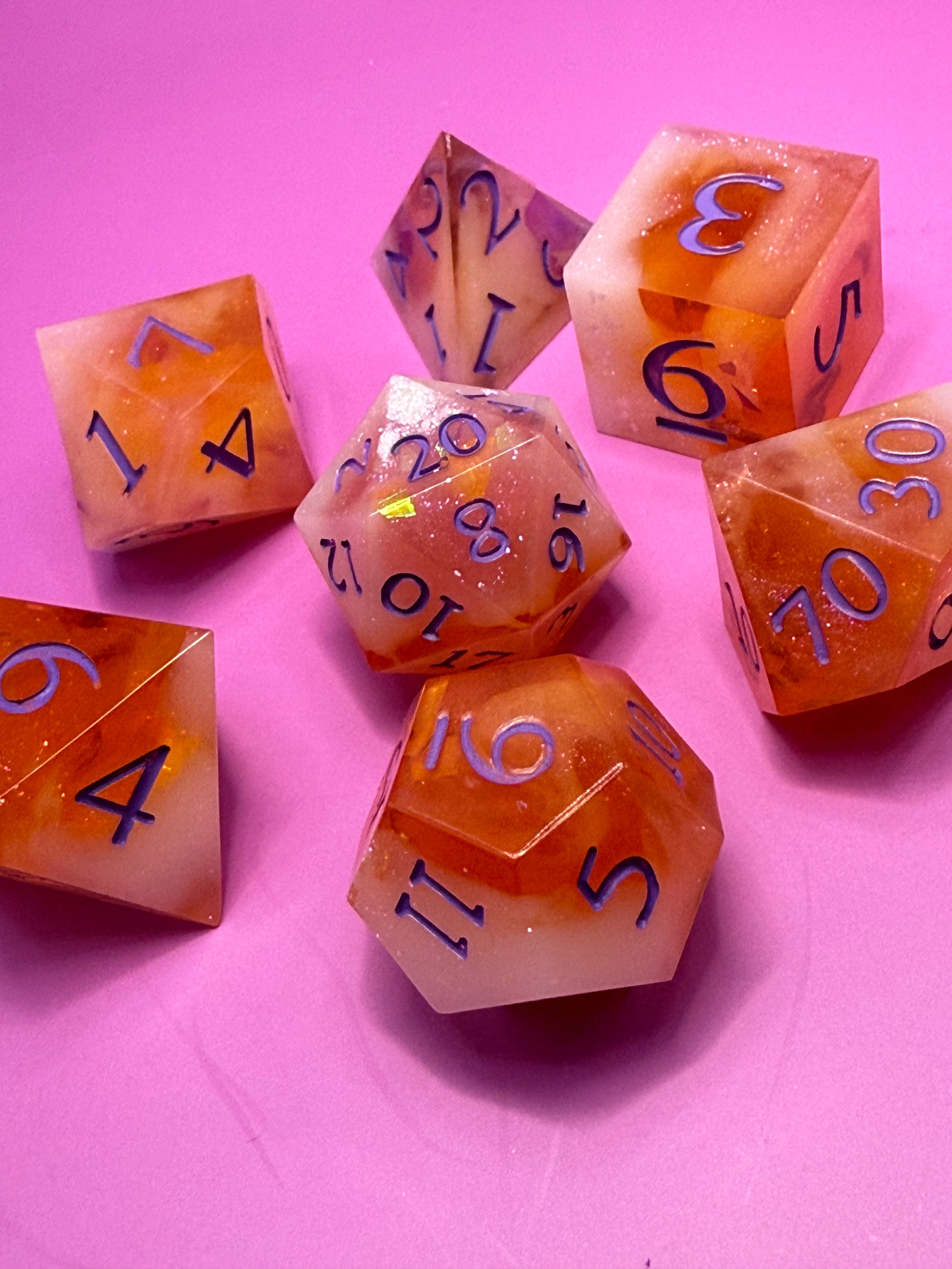 Set of orange polyhedral dice with purple numbers on a pink background