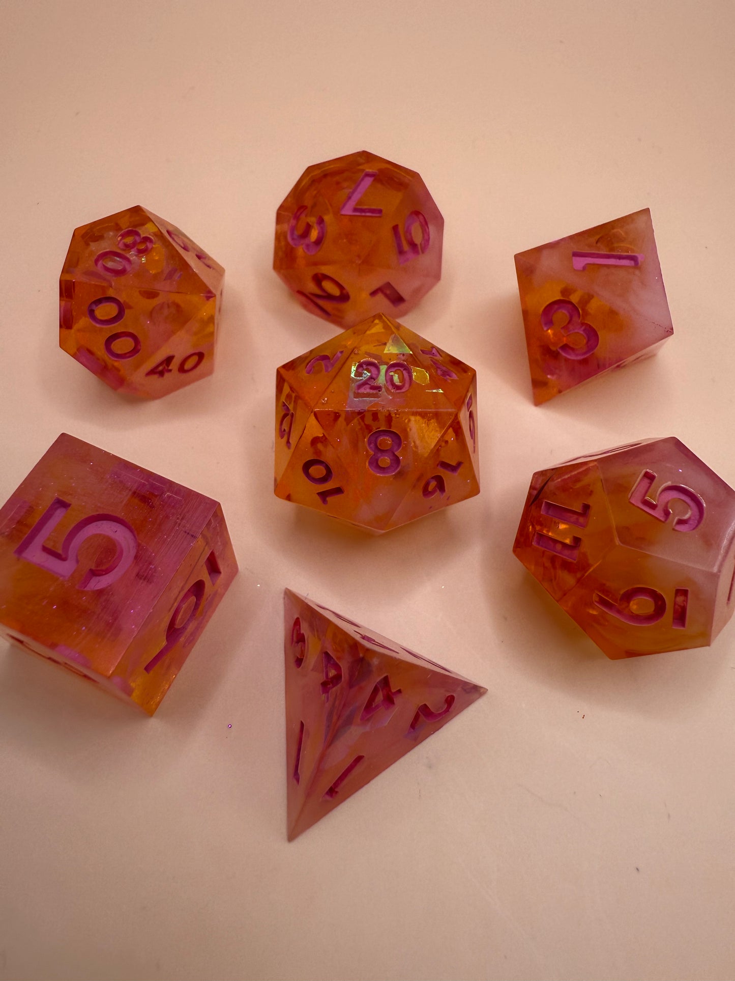 A purple and orange set of seven polyhedral resin dice on a white surface.